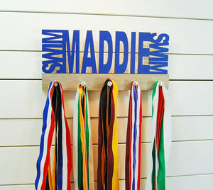 Our personalized swimming medal holder is a great gift for any swimmer so they can display all of their awesome awards. This design comes in a variety of colors, or you can pick from our other choices of sports or phrases so we can customize it just the way you want!