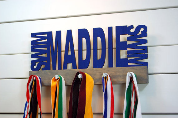  Our personalized swimming medal holder is a great gift for any swimmer so they can display all of their awesome awards. This design comes in a variety of colors, or you can pick from our other choices of sports or phrases so we can customize it just the way you want!