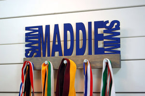 Our personalized swimming medal holder is a great gift for any swimmer so they can display all of their awesome awards. This design comes in a variety of colors, or you can pick from our other choices of sports or phrases so we can customize it just the way you want!
