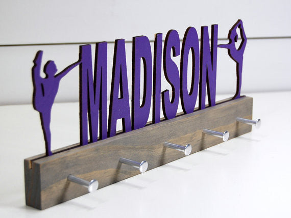 Our personalized dance medal holder is a unique gift for the dancer in your life. This display will be the perfect way for them to show off all of their well-deserved awards. This design comes in a variety of colors, or you can pick from our other choices of sports or phrases so we can customize it just the way you want!