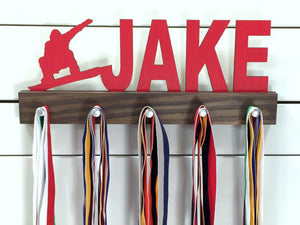 Our personalized snowboarding medal holder is a unique gift for the snowboarder in your life. This display will be the perfect way for them to show off all of their well-deserved awards. This design comes in a variety of colors, or you can pick from our other choices of sports or phrases so we can customize it just the way you want!