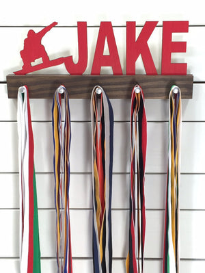 Our personalized snowboarding medal holder is a unique gift for the snowboarder in your life. This display will be the perfect way for them to show off all of their well-deserved awards. This design comes in a variety of colors, or you can pick from our other choices of sports or phrases so we can customize it just the way you want!
