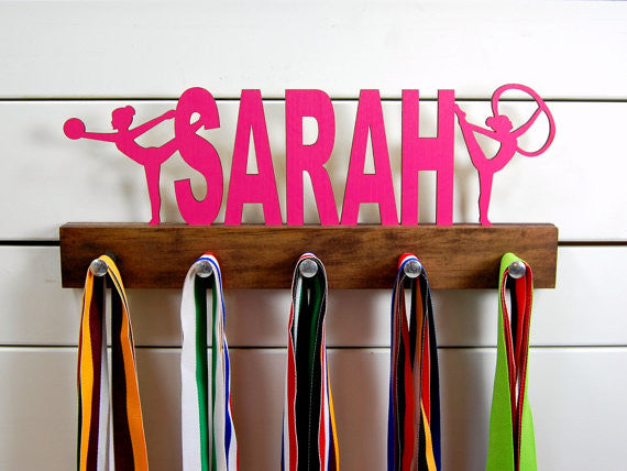  Our personalized rhythmic gymnastics medal holder is a unique gift for the gymnast in your life. This display will be the perfect way for her to show off all of her well-deserved awards. This design comes in a variety of colors, or you can pick from our other choices of sports or phrases so we can customize it just the way you want!