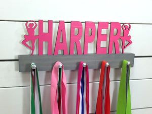 Our personalized ballerina medal holder is a unique gift for the dancer in your life. Whether she has awards to show off or just needs a place to organize her ribbons and jewelry, this display will get the job done. This design comes in a variety of colors, or you can pick from our other choices of sports or phrases so we can customize it just the way you want!