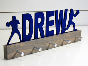 Our personalized football medal holder is a unique gift for the football player in your life. This display will be the perfect way for him to show off all of his well-deserved awards. This design comes in a variety of colors, or you can pick from our other choices of sports or phrases so we can customize it just the way you want!