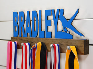 Our personalized gymnastics medal holder is a unique gift for the gymnast in your life. This display will be the perfect way for him to show off all of his well-deserved awards. This design comes in a variety of colors, or you can pick from our other choices of sports or phrases so we can customize it just the way you want!