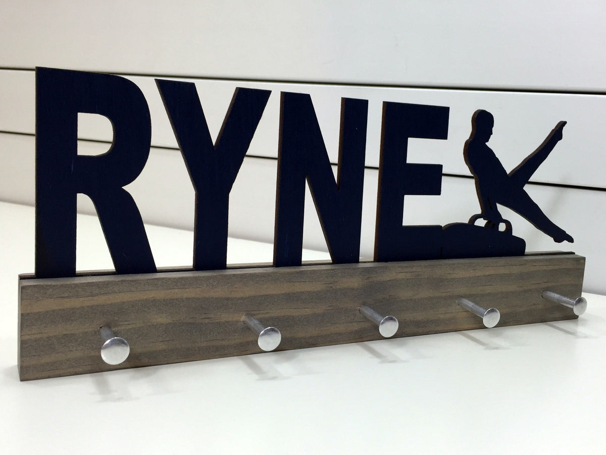 Our personalized gymnastics medal holder is a unique gift for the gymnast in your life. This display will be the perfect way for him to show off all of his well-deserved awards. This design comes in a variety of colors, or you can pick from our other choices of sports or phrases so we can customize it just the way you want!