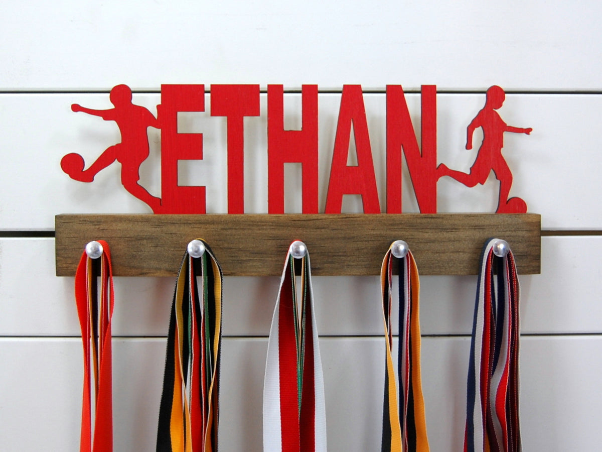 Our personalized soccer medal holder is a unique gift for the soccer player in your life. This display will be the perfect way for him to show off all of his well-deserved awards. This design comes in a variety of colors, or you can pick from our other choices of sports or phrases so we can customize it just the way you want!