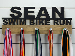  Our personalized triathlon medal holder is a unique gift for any triathlete so they can display all of their awesome and well-deserved awards. This design comes in a variety of colors, or you can pick from our other choices of sports or phrases so we can customize it just the way you want!