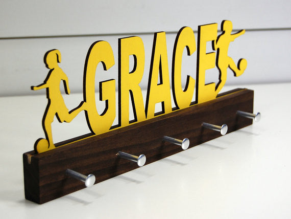 Our personalized soccer medal holder is a unique gift for the soccer player in your life. This display will be the perfect way for her to show off all of her well-deserved awards. This design comes in a variety of colors, or you can pick from our other choices of sports or phrases so we can customize it just the way you want!