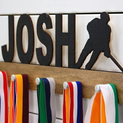  Our personalized hockey medal holder is a unique gift for the hockey player in your life. This display will be the perfect way for them to show off all of their well-deserved awards. This design comes in a variety of colors, or you can pick from our other choices of sports or phrases so we can customize it just the way you want!