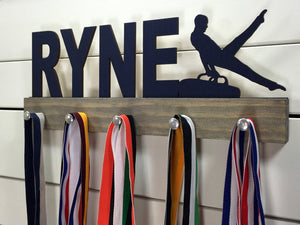  Our personalized gymnastics medal holder is a unique gift for the gymnast in your life. This display will be the perfect way for him to show off all of his well-deserved awards. This design comes in a variety of colors, or you can pick from our other choices of sports or phrases so we can customize it just the way you want!