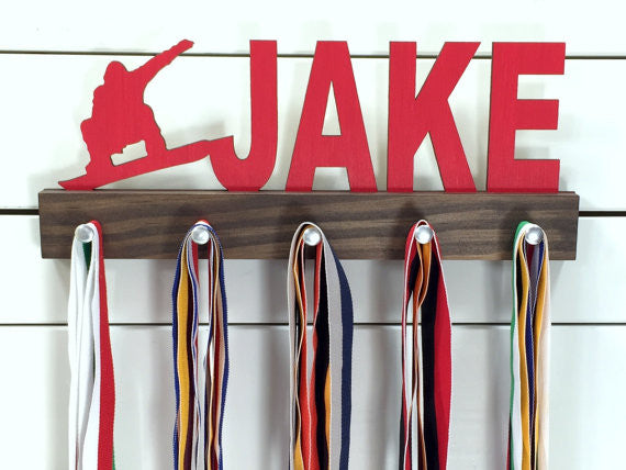  Our personalized snowboarding medal holder is a unique gift for the snowboarder in your life. This display will be the perfect way for them to show off all of their well-deserved awards. This design comes in a variety of colors, or you can pick from our other choices of sports or phrases so we can customize it just the way you want!