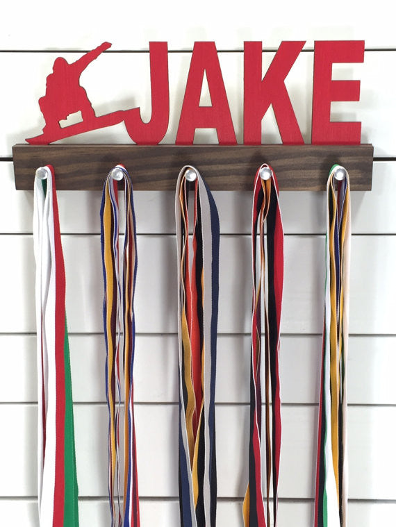  Our personalized snowboarding medal holder is a unique gift for the snowboarder in your life. This display will be the perfect way for them to show off all of their well-deserved awards. This design comes in a variety of colors, or you can pick from our other choices of sports or phrases so we can customize it just the way you want!
